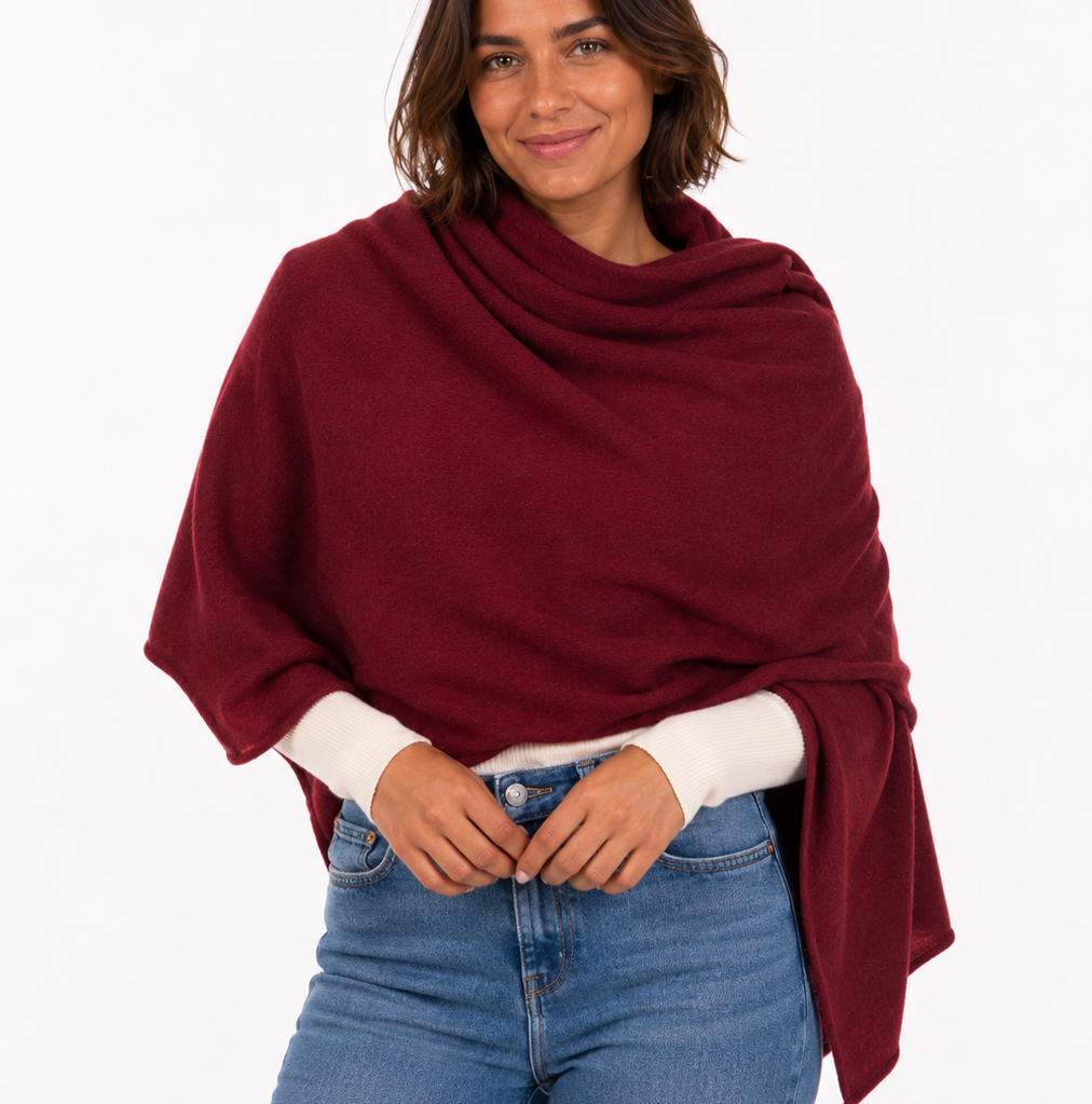 Woman wearing a burgundy poncho over a white shirt and blue jeans on a white background
