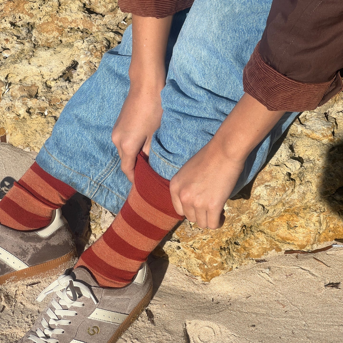 Person wearing striped socks and jeans sitting on a rock