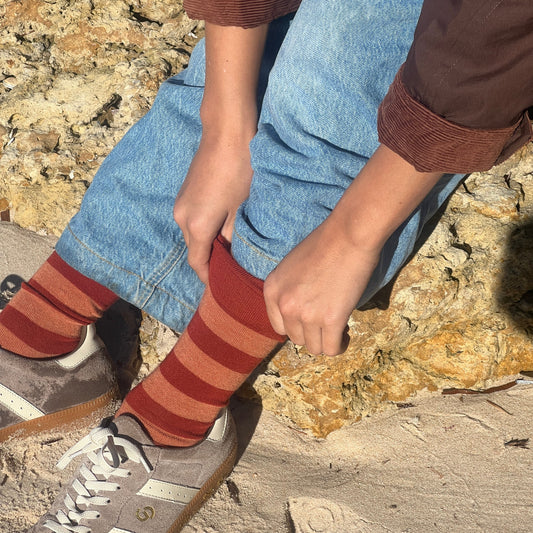 Person wearing striped socks and jeans sitting on a rock